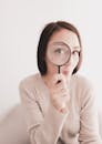 Woman in Beige Sweater Holding Magnifying Glass