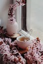白色小杯里，金属泡茶器周围环绕着明亮的粉色小花