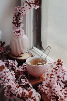 白色小杯里，金属泡茶器周围环绕着明亮的粉色小花