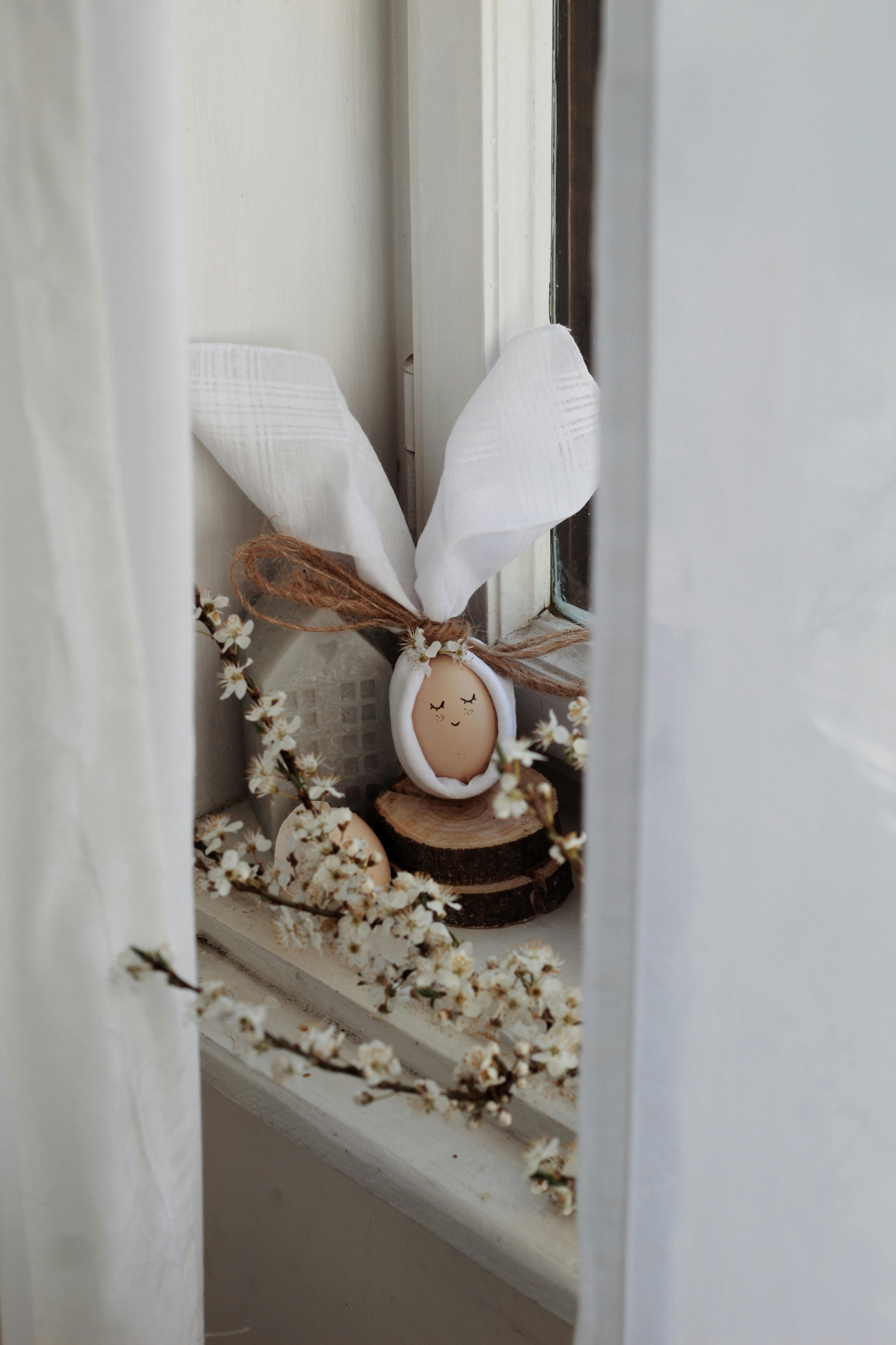 Decorated brown egg near blooming branches with white delicate flowers on windowsill in daylight