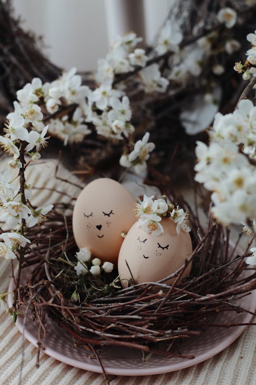Fresh eggs with smiling faces in nest placed on table with flowers for Easter celebration