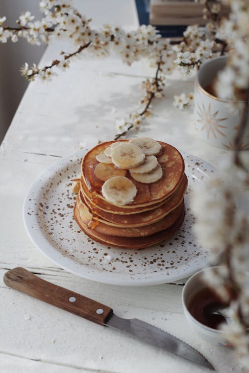 High angle of delicious pancakes garnished with banana slices and caramel topping served on plate in kitchen for breakfast