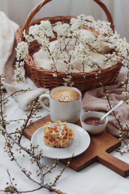 Free Traditional Belgian waffles on plate served with honey and cup of hot cappuccino for breakfast on bed with flowers Stock Photo