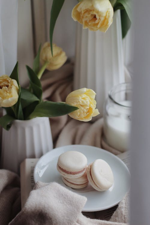 Set of sweet macaroons on plate placed in cozy room with blooming tulip flowers