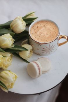 桌上盘子里摆着杏仁饼和黄色郁金香花，旁边是一杯高脚杯装的甜卡布奇诺
