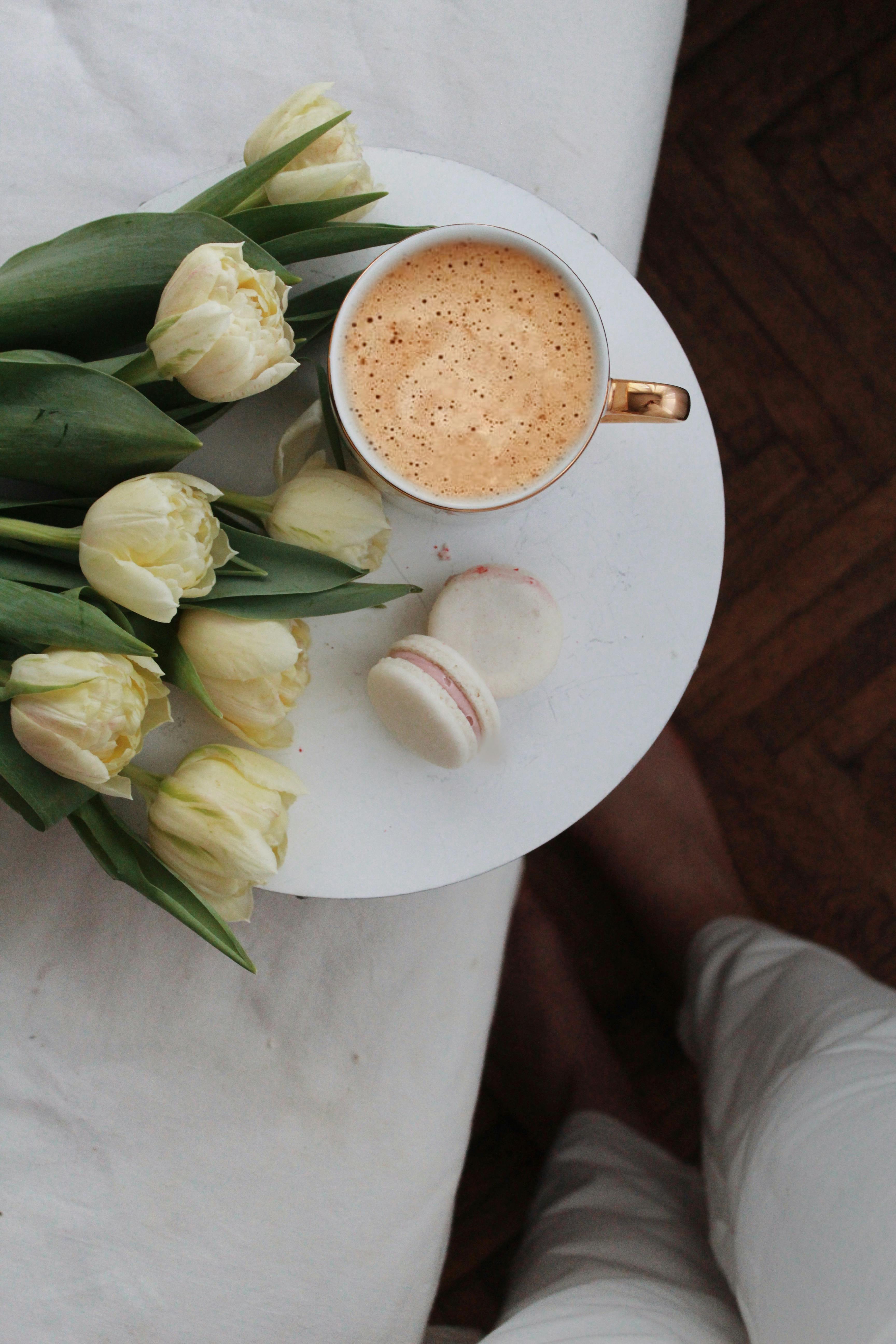 crop woman near bed with coffee and flowers