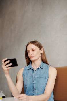 Young woman in a casual denim top looking at her smartphone while sitting indoors.