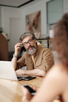 Professional man with glasses working confidently at a laptop in a modern office environment.