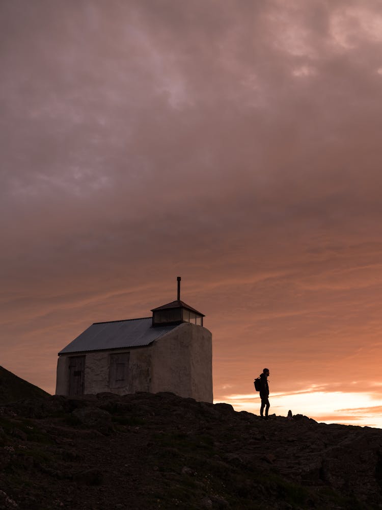 Silhouette Of Person Near Cottage On Overcast Evening