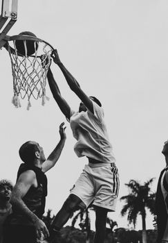 From below black and white of anonymous African American player in sportswear throwing basketball into hoop while playing with multiracial team
