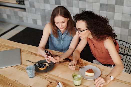 两名女子在一家舒适的咖啡馆里边享用甜点边使用智能手机