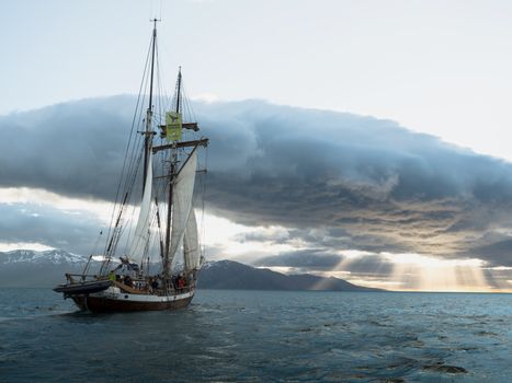 Picturesque scenery of traditional boat with hoisted sails floating on sea against dramatic clouds during sunset
