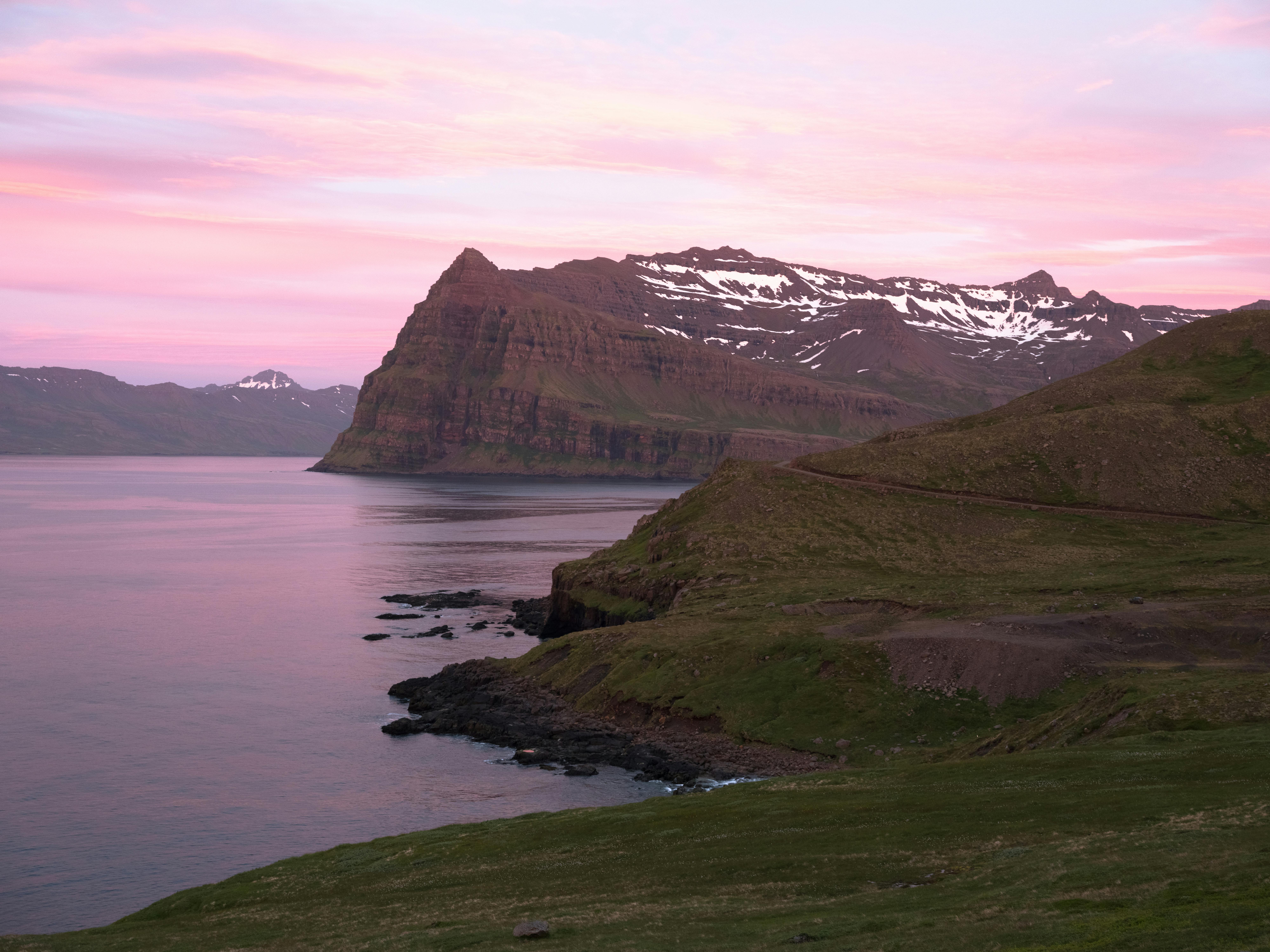 Picturesque pink sunset sky reflecting in surface of calm sea surrounded by rocky mountains