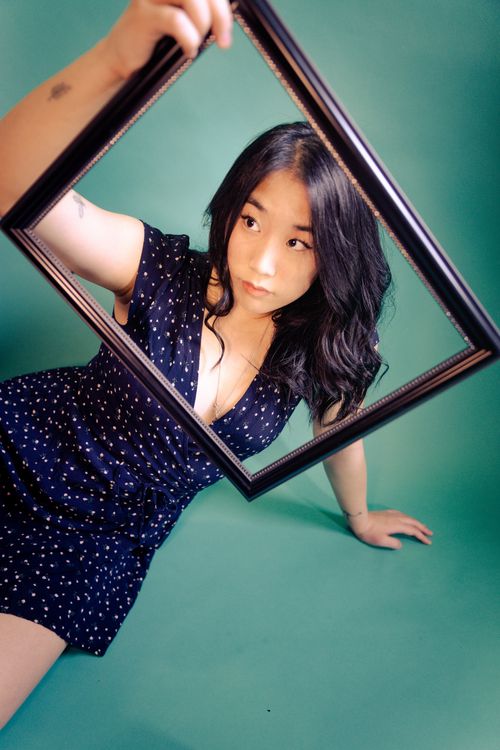 Free Stylish portrait of an Asian woman holding a frame against a vibrant green backdrop, capturing elegance and creativity. Stock Photo