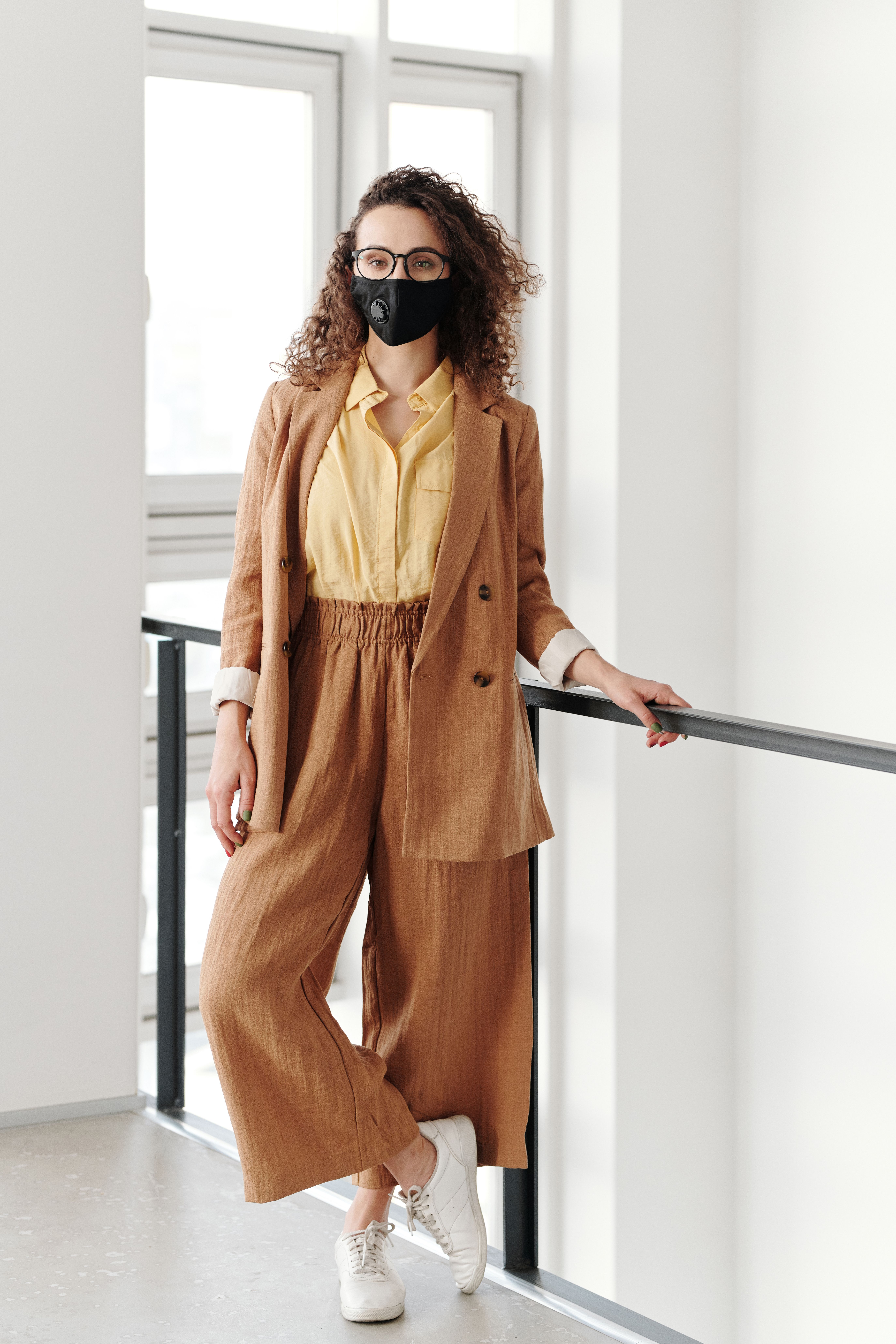 Elegant woman wearing a mask and stylish outfit, standing indoors, promoting safety and fashion.