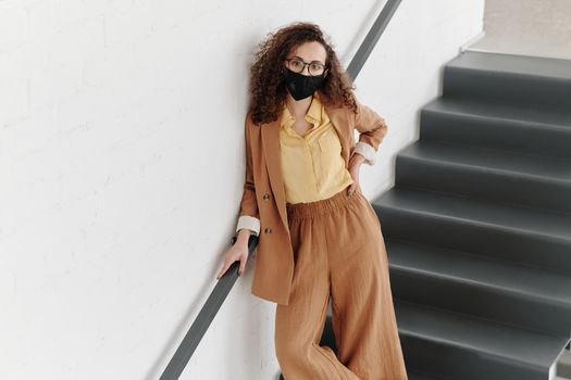 一位戴着口罩、身着时尚服装的女性在室内楼梯上摆姿势拍摄现代肖像