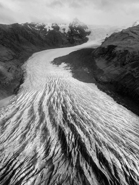 Drone view of wild glacial river streaming through mountainous terrain in foggy winter day