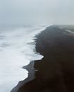 无人机视角下，阴天的黑色火山海滩上翻滚着泡沫海浪