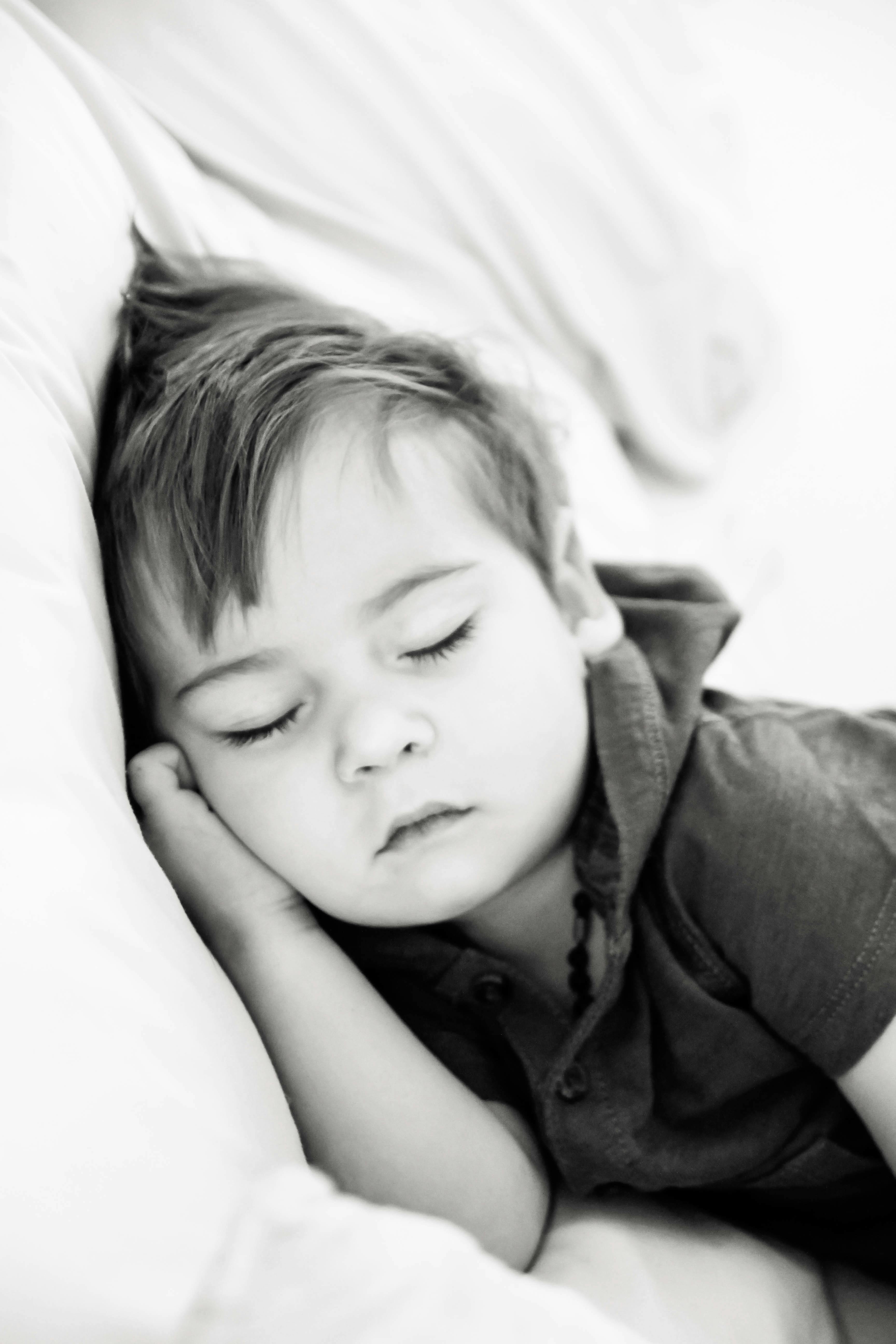 grayscale photography of a little boy sleeping on bed