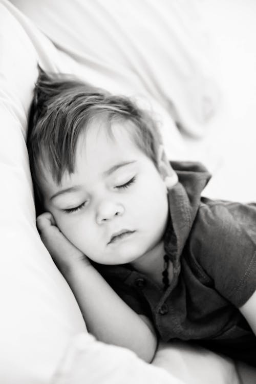 Grayscale Photography of a Little Boy Sleeping on Bed