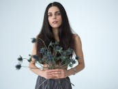 一位深色长发的美丽年轻女性，手捧一束海冬青花，注视着镜头