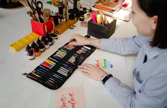 Woman organizing art supplies in a creative workspace focused on calligraphy and lettering.