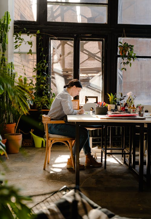 Photo of Woman Sitting by the Table While Writing