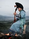 Side view of thoughtful Mongolian male musician in traditional costume sitting on stool in valley and playing morin khuur musical instrument