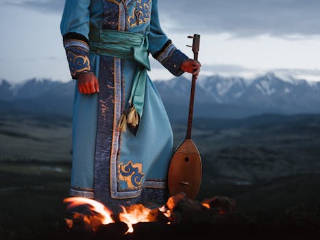 A traditional musician in ornate attire plays an instrument by a bonfire against a mountainous backdrop at dusk.