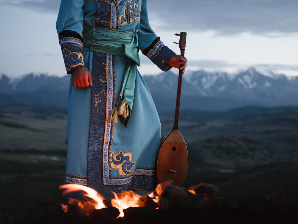 Crop person standing near bonfire with Mongolian folk instrument in valley