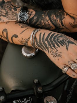 Crop of unrecognizable brutal man with different tattoos rings bracelets and clock placed on motorbike during relaxing