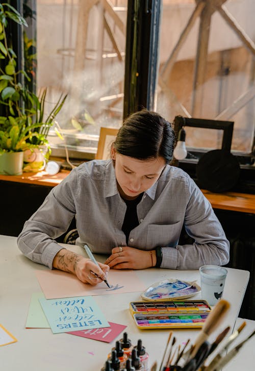 Woman in Gray Button Up Shirt  Writing on Pink Paper