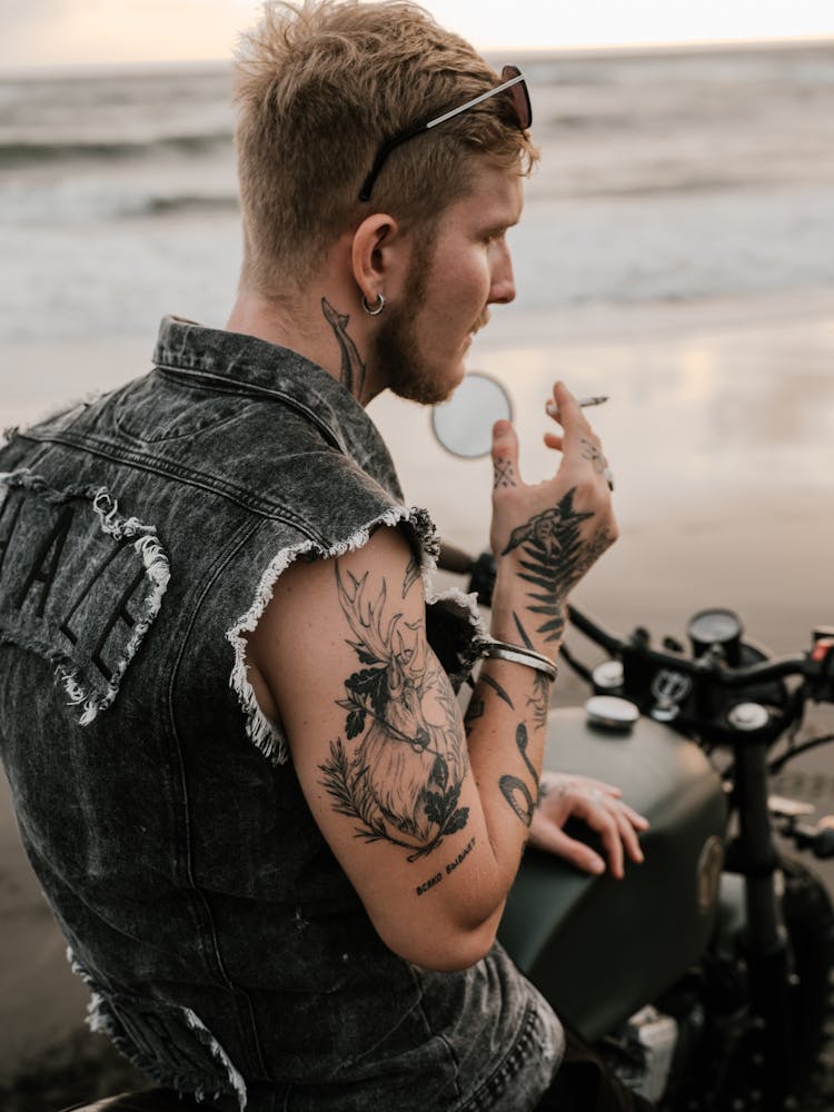 Tattooed Biker Smoking Cigarette On Motorcycle On Sea Coast