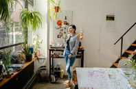 阳光明媚的工作室里，一名妇女拿着马克杯站在植物和艺术品中间