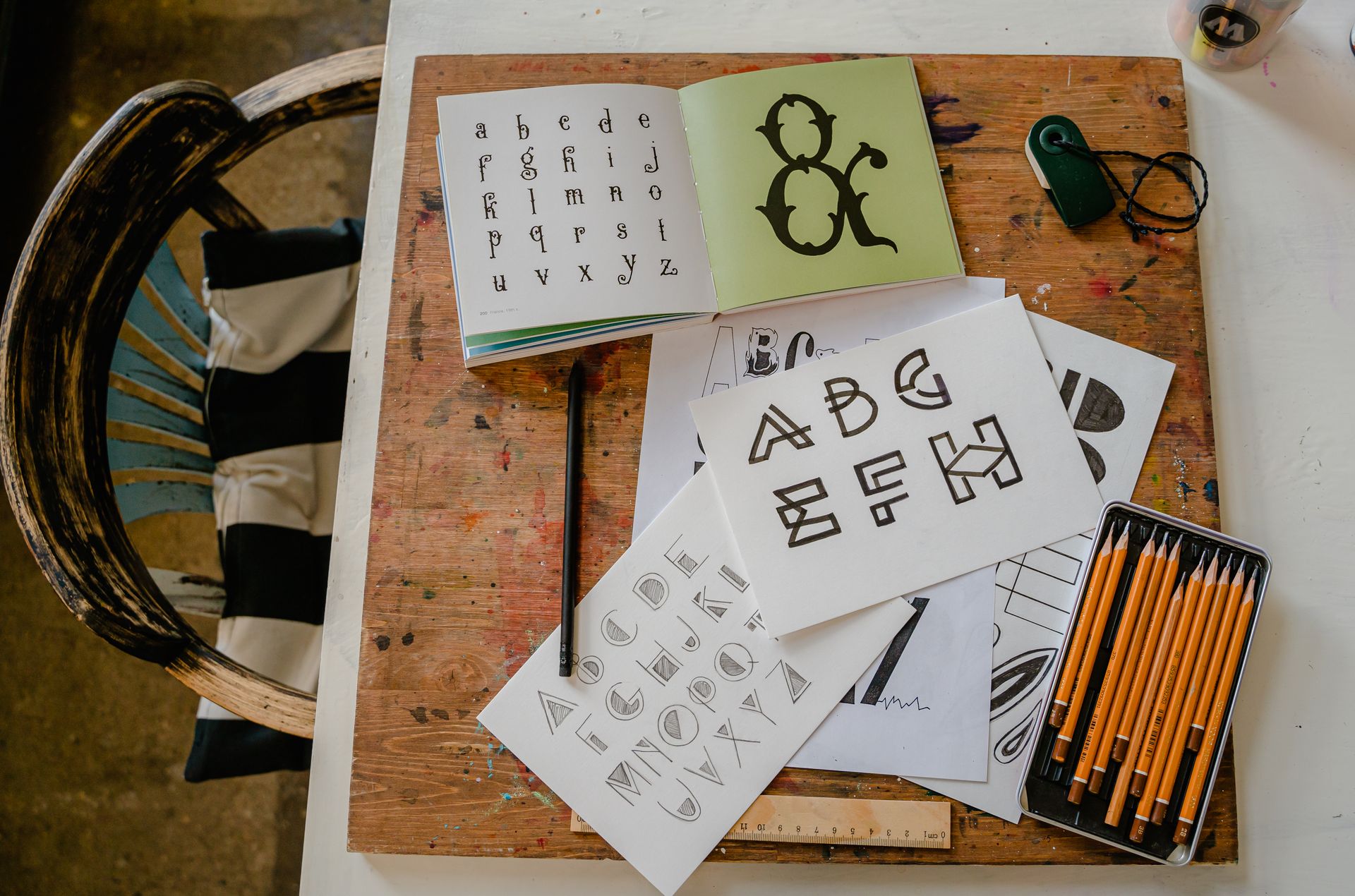 A top-down view of calligraphy tools and alphabets on a wooden table for creative lettering projects.
