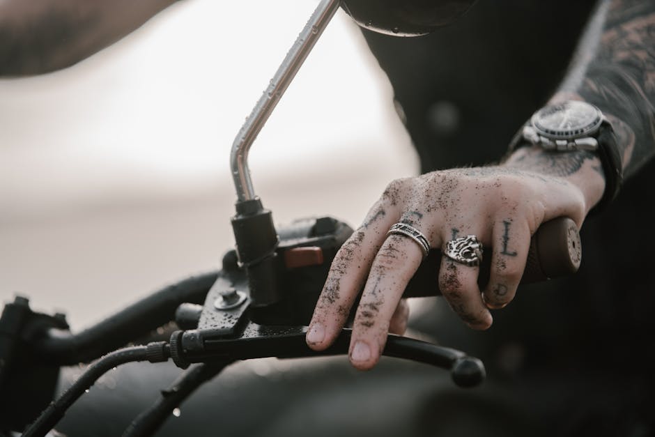 Crop faceless male hipster in silver rings on dirty fingers and wristwatch riding modern motorbike with metal and plastic pieces covered with drops