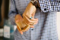 Crop unrecognizable male in checkered shirt holding parchment paper with cannabis and milling hemp with scissors while standing in daylight