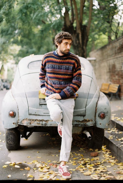 Male model standing leaned on old car near sidewalk