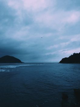 A tranquil seascape featuring a calm ocean under a dramatic cloudy sky.