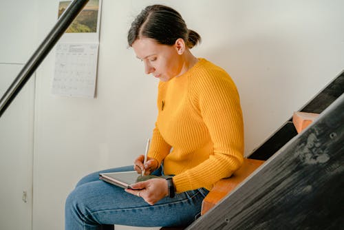 Woman in Yellow Sweater and Denim Jeans Sitting on Stairs