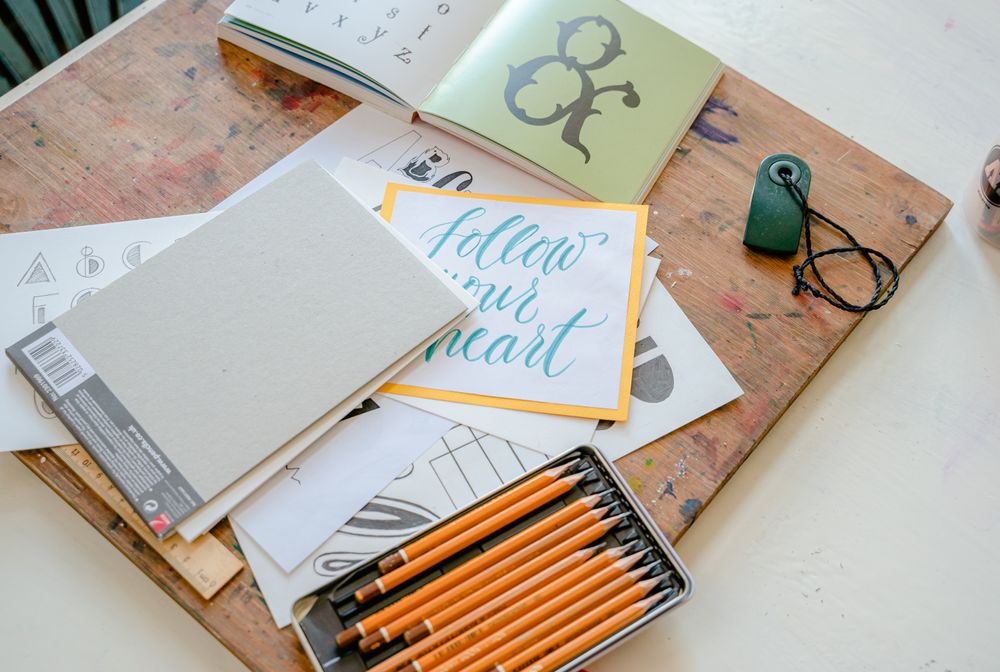 Pencilled lettering layout on paper surrounded by pens and an eraser — photo by Adventure Studio on Pexels