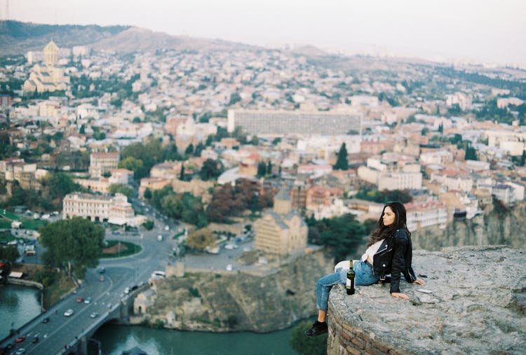 A Lonely Woman Sitting On A Cliff Overlooking The City