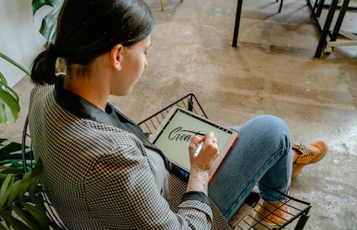Woman Sitting on Black Metal Chair Using a Tablet