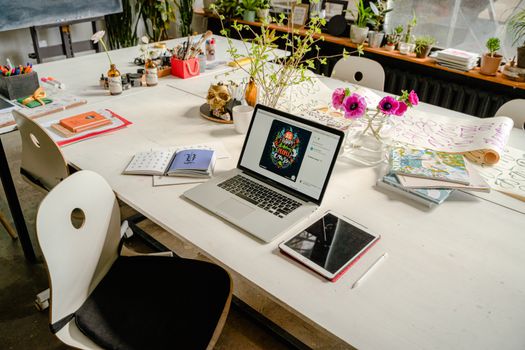 Artistic workspace featuring a laptop, tablet, flowers, and art supplies on a table.