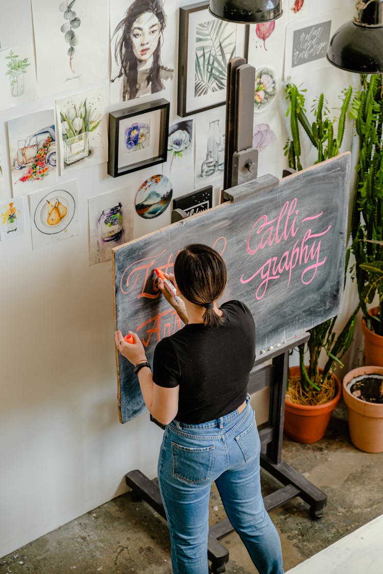 Woman In Black Shirt And Blue Denim Jeans Writing On The Chalkboard