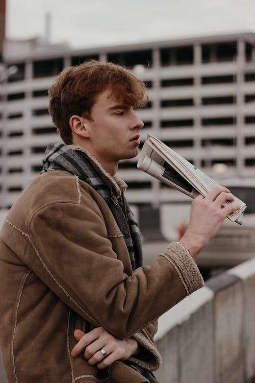 Man in Brown Jacket and Gray Muffler Holding a Newspaper