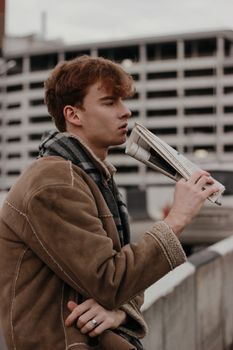 一名成年男子在户外的混凝土建筑旁，拿着报纸，若有所思