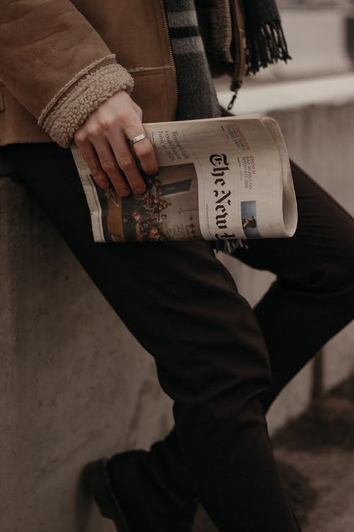 Person in Brown Coat Holding White and Black Labeled Bottle