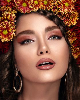 Crop face of sensitive female model with open mouth and bright makeup with flowers on head and earrings looking at camera
