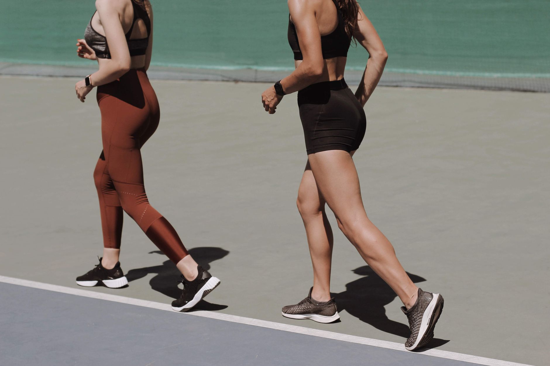 Two women walking on an outdoor track in sportswear, emphasizing healthy lifestyle and fitness.